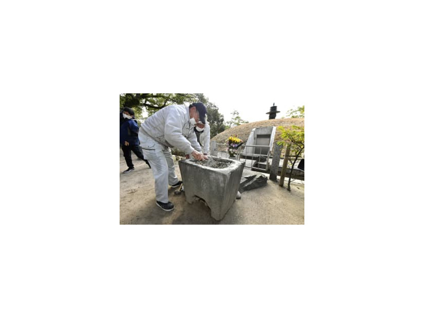 セメントのようなもので埋められた鉢の修復作業。奥は原爆供養塔＝20日午前、広島市の平和記念公園