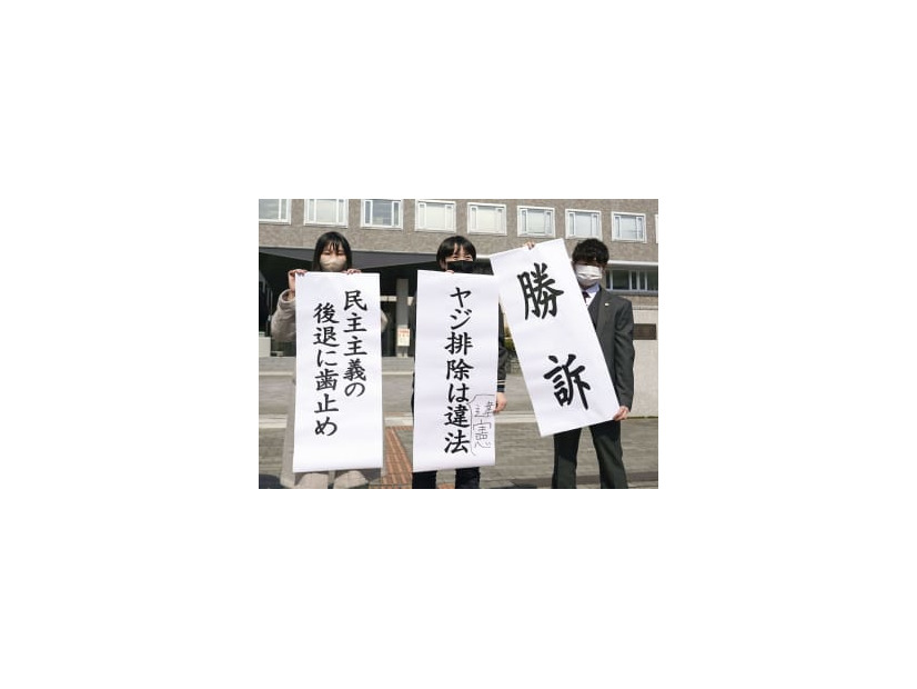 札幌地裁前で「勝訴」などと書かれた紙を掲げる原告側＝25日午前