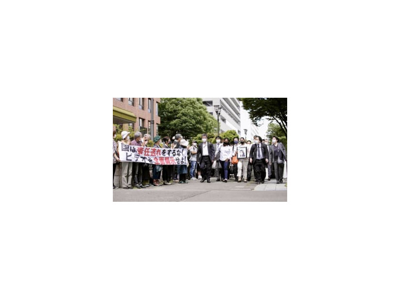 第1回口頭弁論のため、名古屋地裁に向かう遺族ら原告団。左は横断幕を掲げる支援者ら＝8日午後、名古屋市