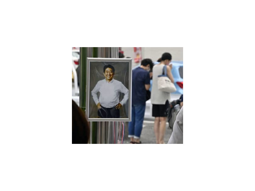 献花台に飾られた安倍元首相の写真。奥は銃撃された現場近くで手を合わせる人たち＝7月15日、奈良市