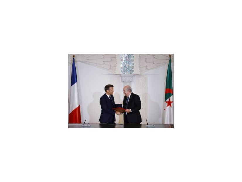 27日、アルジェで握手するアルジェリアのテブン大統領（右）とフランスのマクロン大統領（AP＝共同）