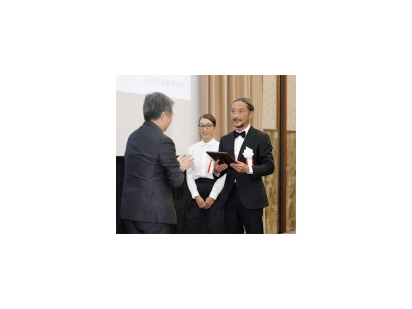 地域貢献大賞を受賞し、日本新聞協会の丸山昌宏会長（左）から表彰される長崎新聞青方販売センターの芳賀良介所長と妻佳美さん＝17日午後、東京都内