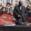「汚染を少なく、さらなる解決策を」と書かれたボードを抱える子どもの横で、排出基準規則に署名する米環境保護局のリーガン長官（右）＝20日、ワシントン（AP＝共同）