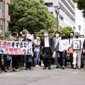 第1回口頭弁論のため、名古屋地裁に向かう遺族ら原告団。左は横断幕を掲げる支援者ら＝8日午後、名古屋市