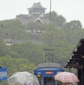 傘を差して熊本市内を歩く人たち。上は熊本城＝5日午前8時11分