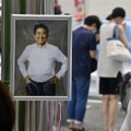 献花台に飾られた安倍元首相の写真。奥は銃撃された現場近くで手を合わせる人たち＝7月15日、奈良市