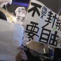 JR新宿駅周辺でメッセージを掲げ、中国共産党の独裁的な統治に抗議する在日中国人ら＝30日夜、東京都新宿区