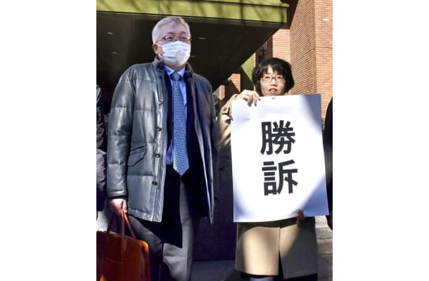「勝訴」と書かれた紙を掲げる弁護士と原告の奥田恭正さん＝18日午後、名古屋地裁前