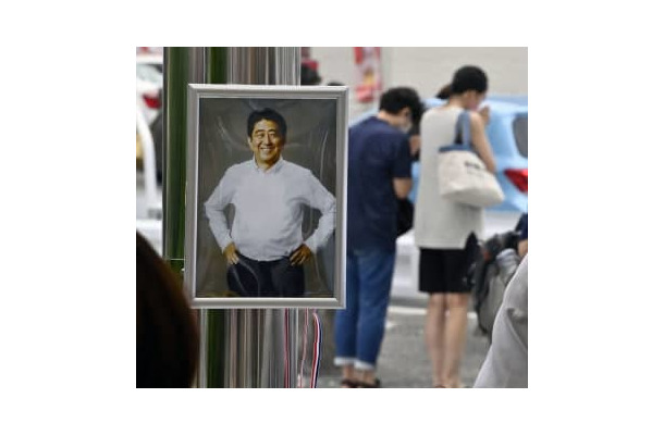 献花台に飾られた安倍元首相の写真。奥は銃撃された現場近くで手を合わせる人たち＝7月15日、奈良市