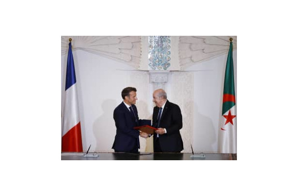 27日、アルジェで握手するアルジェリアのテブン大統領（右）とフランスのマクロン大統領（AP＝共同）