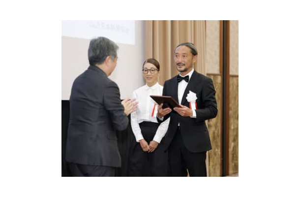 地域貢献大賞を受賞し、日本新聞協会の丸山昌宏会長（左）から表彰される長崎新聞青方販売センターの芳賀良介所長と妻佳美さん＝17日午後、東京都内